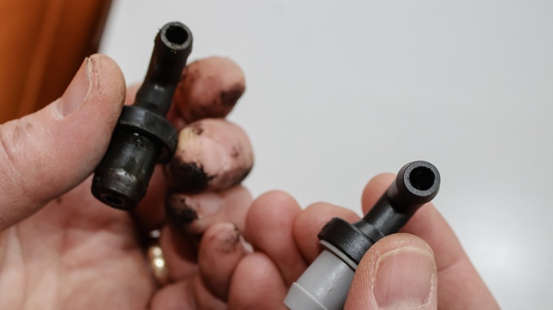 Two hands holding old and new PCV valves