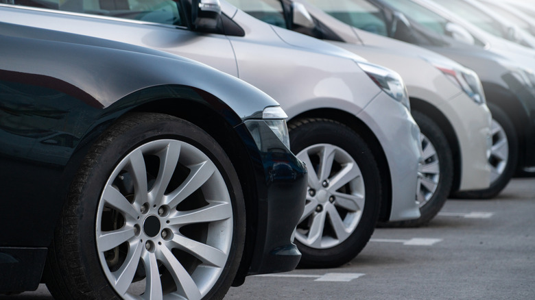 A line of black, grey, and silver sedans parked in a row with passenger front wheels visible