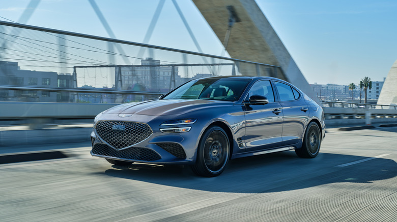 A silver 2026 Genesis G70 being driven on a bridge.