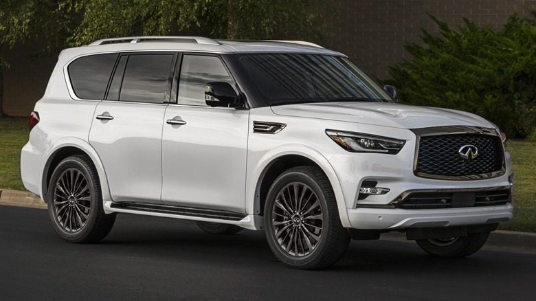 A white 2021 Infiniti QX80 parked by a tree and a brick building.