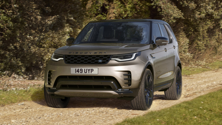 A gold 2021 Land Rover Discover on an unpaved road in front of trees.