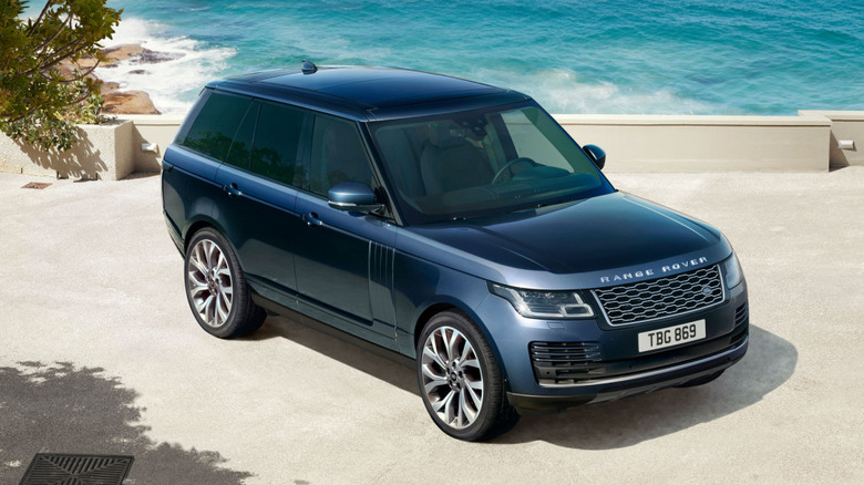 A blue 2021 Land Rover Range Rover on a beach with a seawall and crashing waves behind it.