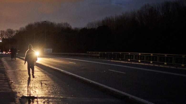 A Person walking along a highway facing traffic