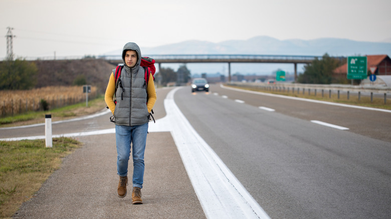 A man with a backpack walking along highway