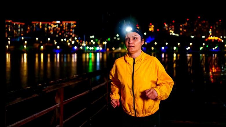A woman running at night wearing reflective jacket and headlamp