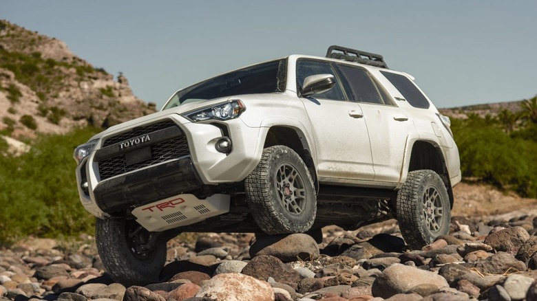 A white 2021 Toyota 4Runner being driven over rocks with hills in the background.
