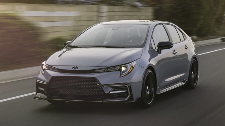A gray 2021 Toyota Corolla Sedan in motion on a roadway with a wall in the background.