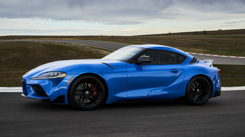 A left-side profile shot of a blue 2021 Toyota GR Supra being driven on a track.