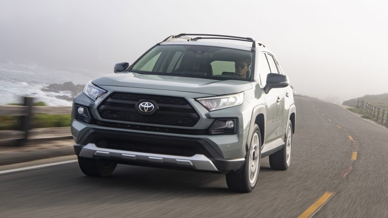 A gray 2021 Toyota RAV4 being driven on a two-lane roadway alongside a rocky shoreline.