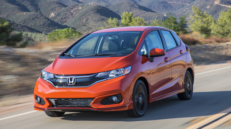 An orange 2019 Honda Fit hatchback seen in left front three-quarter view driving with hills in background