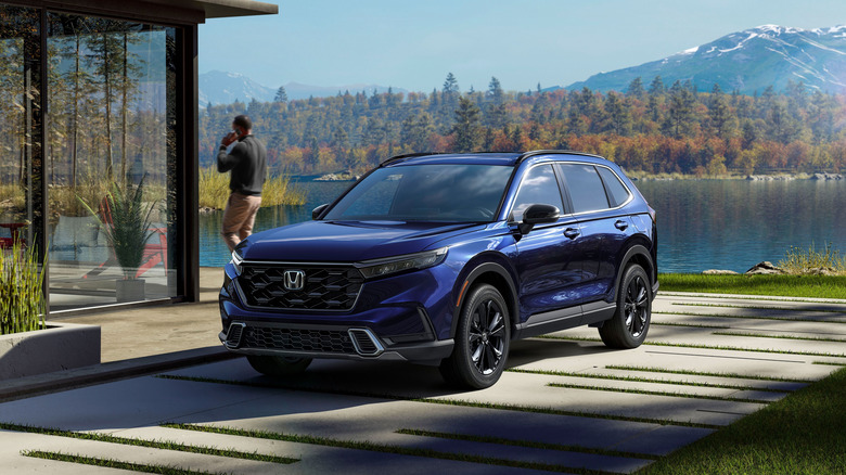 A blue 2024 Honda CR-V Sport Touring SUV seen in left front three-quarter view parked by a mountain lake