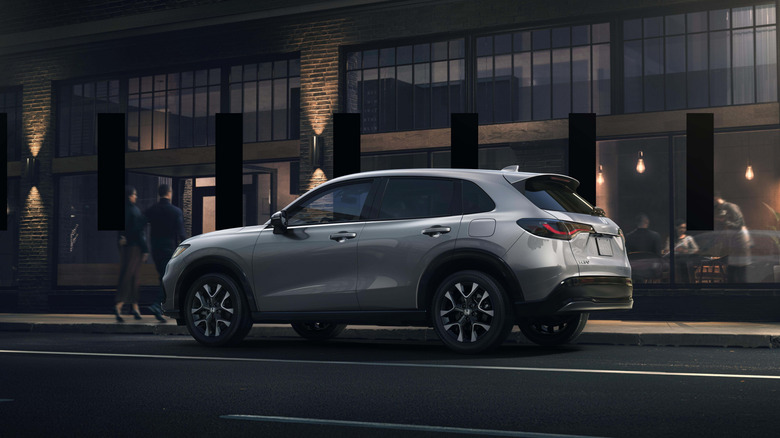 A gray 2026 Honda HR-V SUV seen from left rear three-quarter view parked in a sophisticated city street scene
