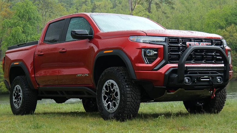 A red 2023 GMC Canyon AT4X parked on grass next to a body of water