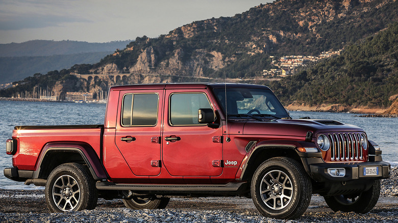 A dark red Jeep Gladiator on a rocky beach in front of a steep incline