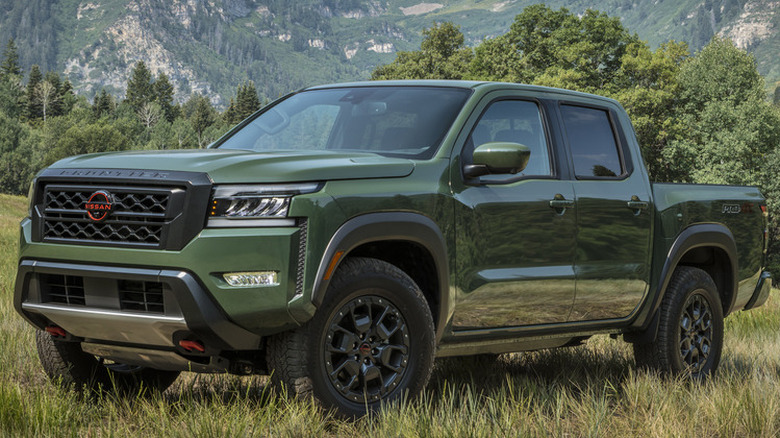 A green Nissan Frontier parked on grass in front of bushes