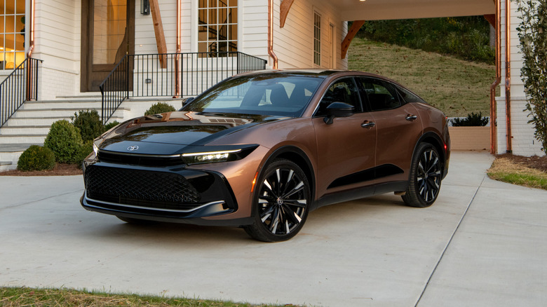 Bronze-colored Toyota Crown sedan left front quarter view parked in front of a luxurious house