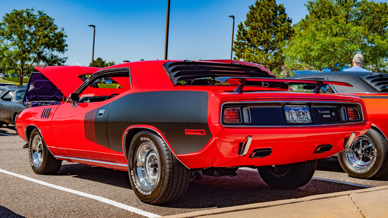 A red Plymouth 'Cuda shows its rear window louvers from the rear in a parking lot.