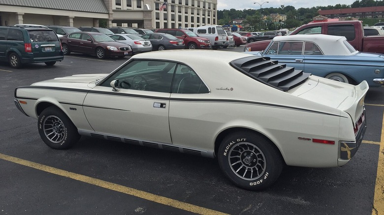 A white 1970 AMC Javelin SST shows its rear window louvers in a parking lot.