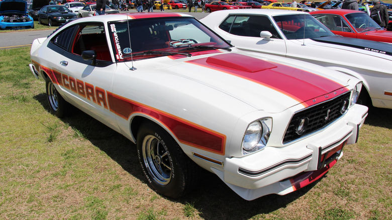 A Mustang II in red and white is shown from the front with side-window louvers visible.