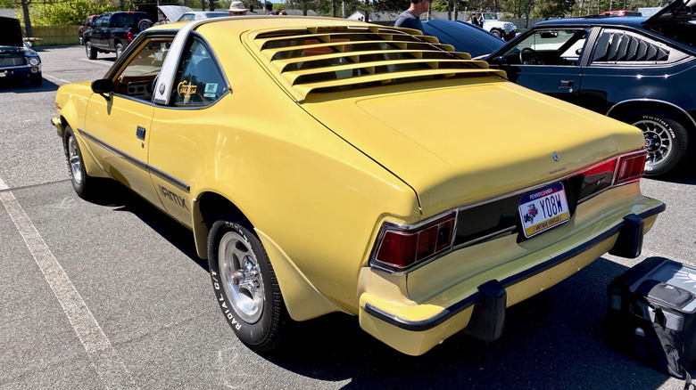 A yellow 1977 AMC Hornet AMX shows color-matched rear window louvers from behind.