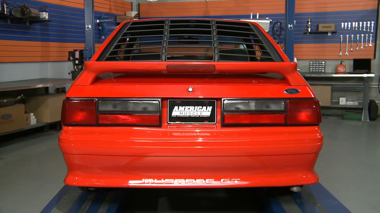 A red Ford Mustang Fox Body is shown from the rear with black window louvers.