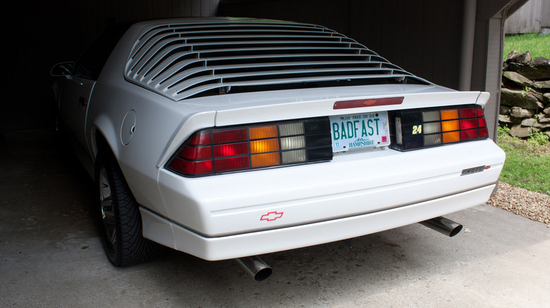 The front of a white Camaro is obscured in shadows while the rear shows color-matched rear window louvers.