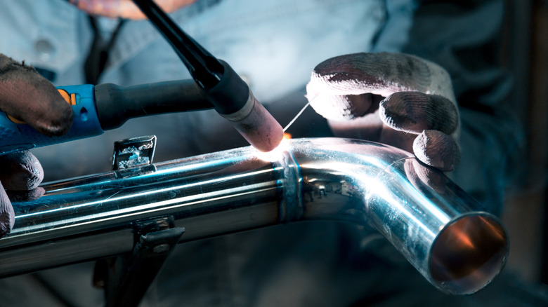 A close-up shot of a worker TIG welding two metal pipes together.