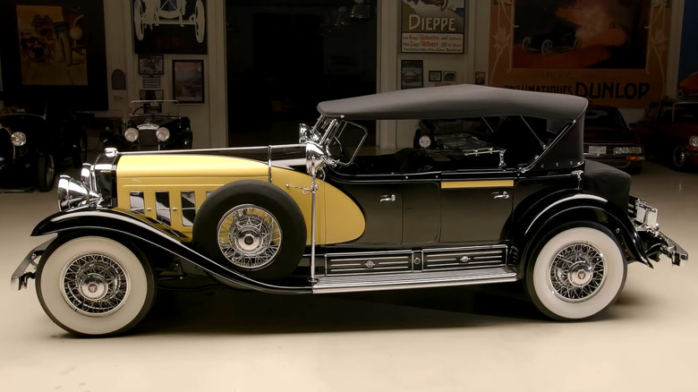 A 1930 Cadillac V16 Convertible Sedan finished in yellow and black standing in a garage with other rare cars in the background.