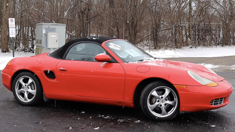 A red Porsche Boxster is parked in the snow.