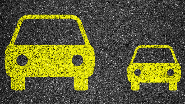 A large car and a small car are depicted in parking lot paint.