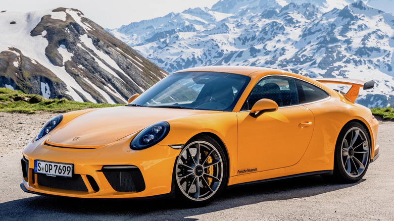 An orange Porsche 911 sits among snowy mountains.
