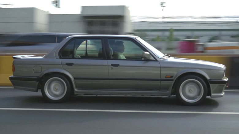 A BMW E30 325i drives on the highway.
