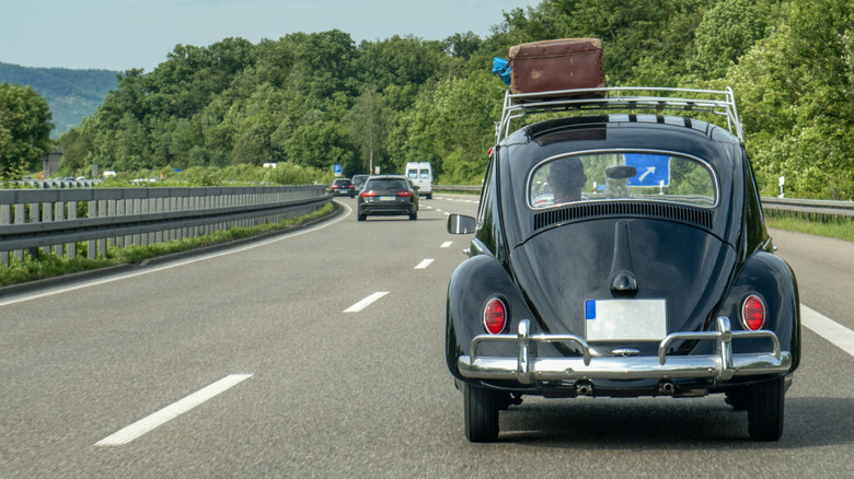 A black VW Beetle drives down a highway.