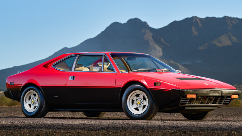 Ferrari Dino 308 GT4 sits parked outside with mountains in background.