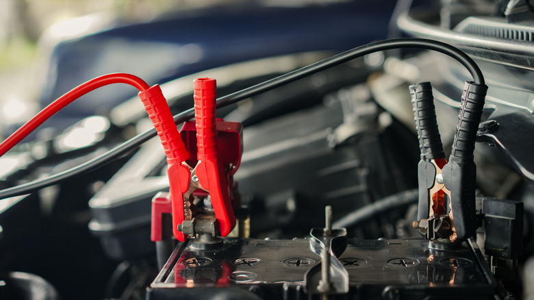 Red and black booster cable clamps connected to terminals of a car battery.