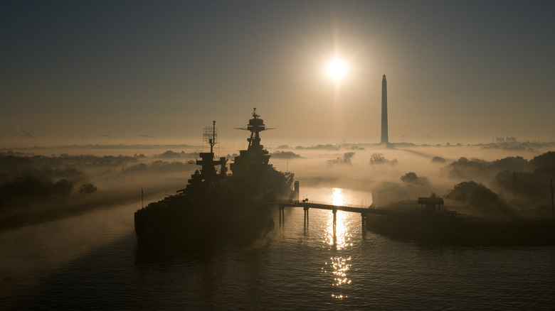 Battleship USS Texas seen from a high distance front port side view in morning fog with San Jacinto Monument in  background