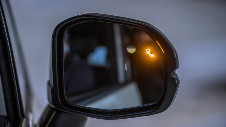 A car's rearview mirror showing an illuminated blind spot assist warning.