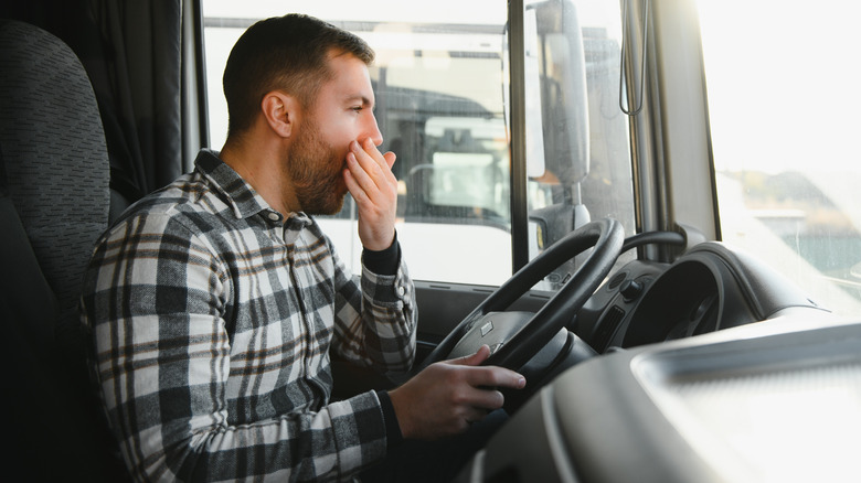 A male driver behind a steering wheel of a truck yawning.