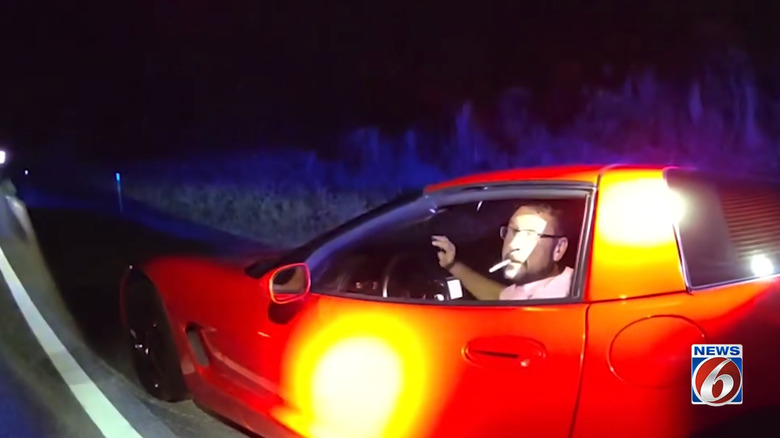 A screenshot of body cam footage obtained during Signorino's traffic stop and arrest showing the man sitting in his red 1998 Chevrolet Corvette and smoking a cigarette while speaking with authorities.