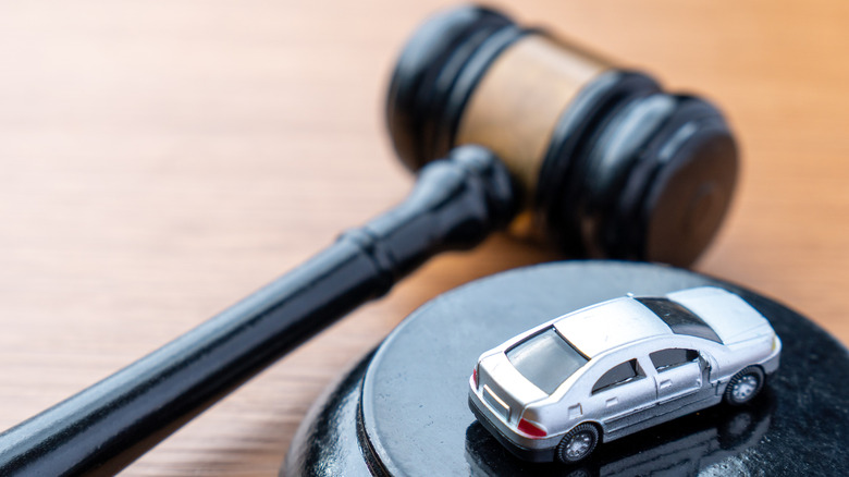 A gavel and hammer, with a small, silver toy car, sits on a wood desktop.