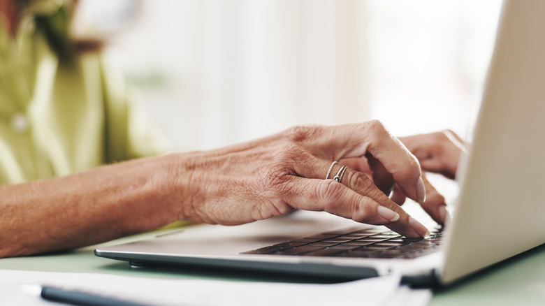 Older woman's hands typing on a laptop keyboard.