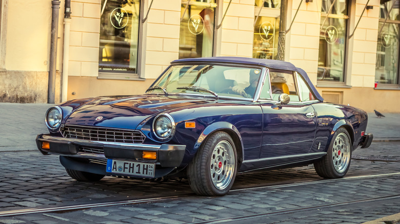 A Blue 1980 Fiat 124 Spider pictured on a cobblestone street.