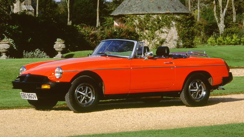 A red 1980 MG B Roadster is pictured on a gravel parkway.