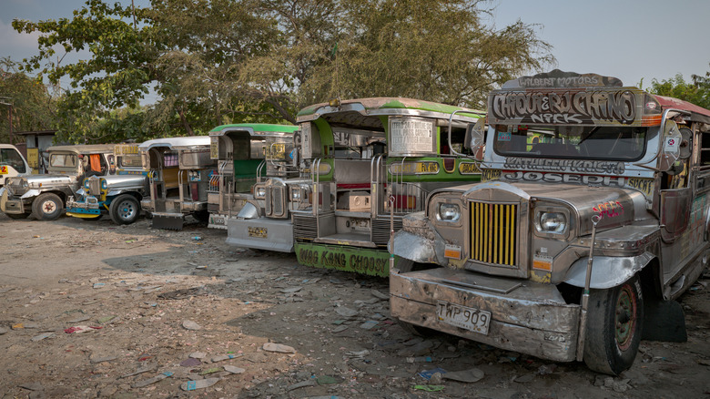 Jeepneys in the Philippines parked in a dirt lot waiting for service.