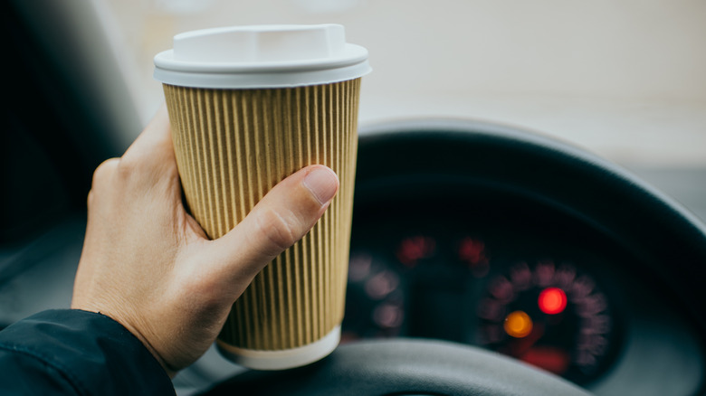A coffee cup rests on the top of a steering wheel.