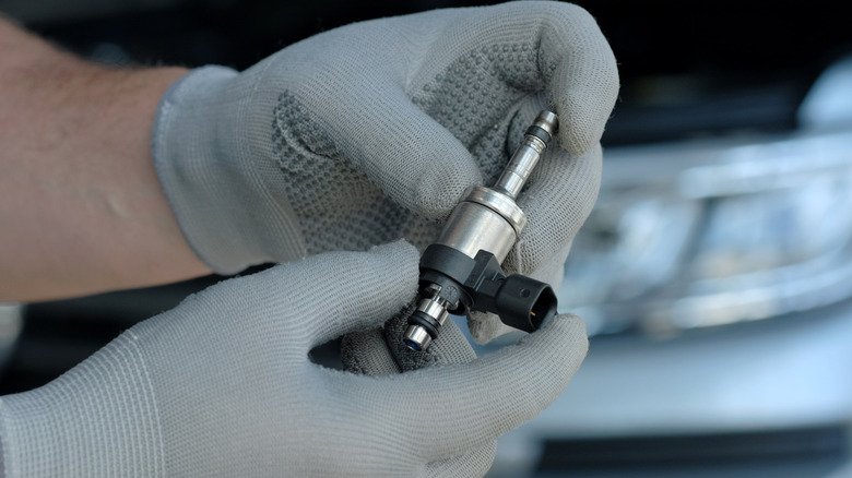 Gloved hands hold a fuel injector.