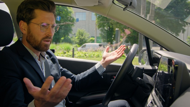 A bearded driver holds his hands up in confusion.