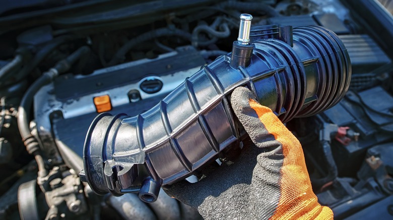 A gloved hand examines intake components.