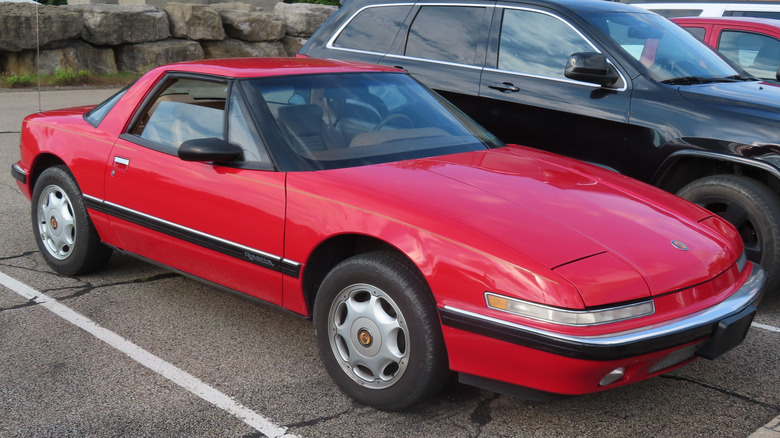 A red Buick Reatta sits parked in a lot, front three-quarter view.