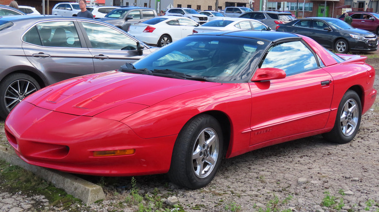 A red 1997 Pontiac Firebird Coupe parked amongst many other cars, front three-quarter view.